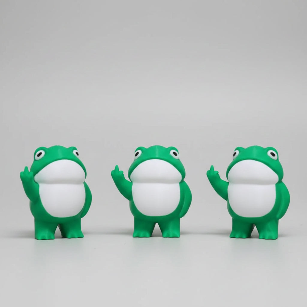 Three green frog figurines with white bellies on a concrete surface.