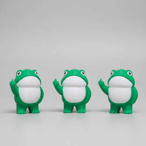 Three green frog figurines with white bellies on a concrete surface.