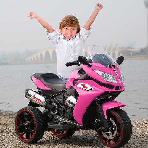 Child with arms raised next to a pink toy motorcycle by a water body