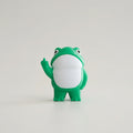Green frog figurine on a yellow surface with a white background